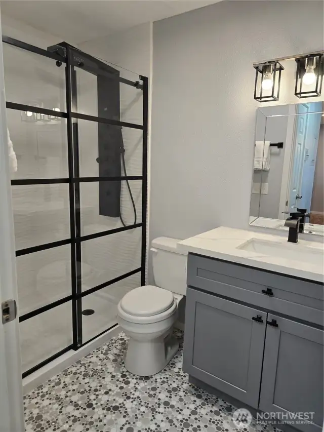 Upgraded bathroom includes a glass shower door, 8 spout shower head, tile to the ceiling in the shower, custom tiles on the floor and new cabinet with quartz top and all new fixtures.