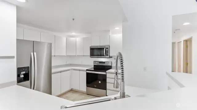 Kitchen features white sleek cabinetry and new stainless steel appliances.