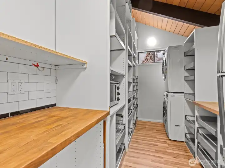 Nearby, the massive walk-in pantry and built in storage shelves with pull out drawers. You'll have plenty of space in here for all of your non-perishable items, coffee maker or tea kettle, air fryer and more. The upstairs washer and dryer is also tucked in at the back. A pocket door closes off the space for a cleaner look.