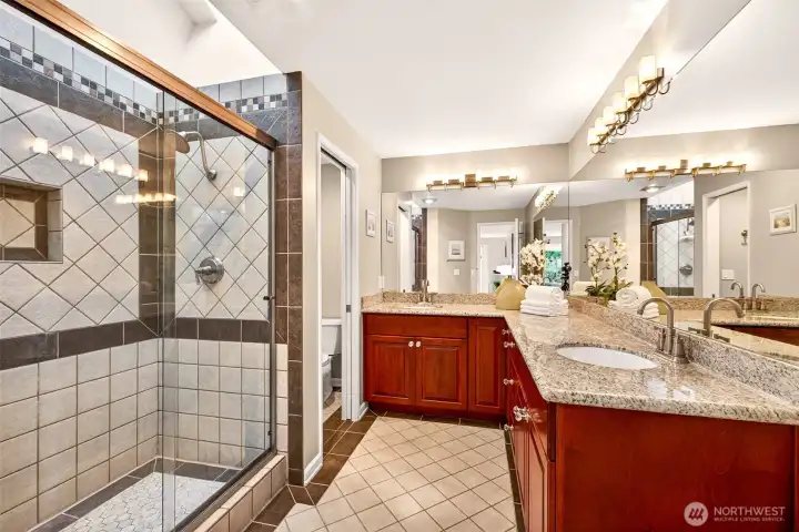 The primary bath feels spacious and bright, with an extended granite dual sink vanity, rich cabinetry, and generous mirror and lighting, plus a separate tile shower and a private water closet.