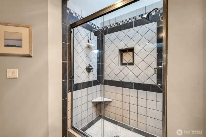 A closer look at the shower highlights the custom tilework, frameless glass enclosure, built in niche, and a corner shelf for everyday comfort.