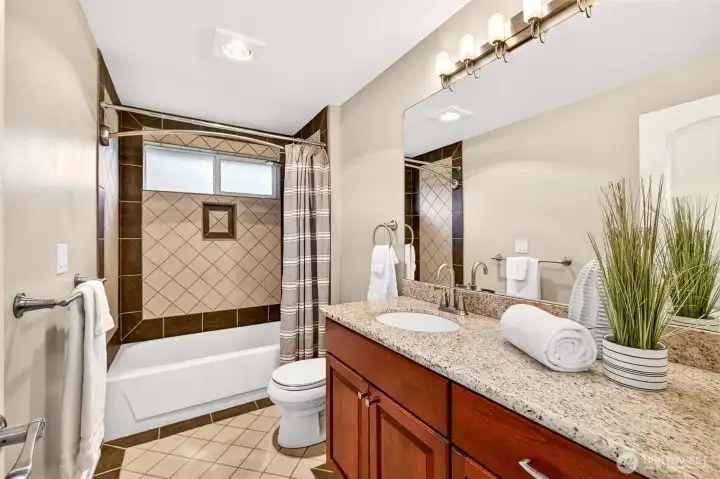 Updated full bath with granite counter, modern fixtures, and a tiled tub surround, plus high windows that bring in natural light while maintaining privacy.