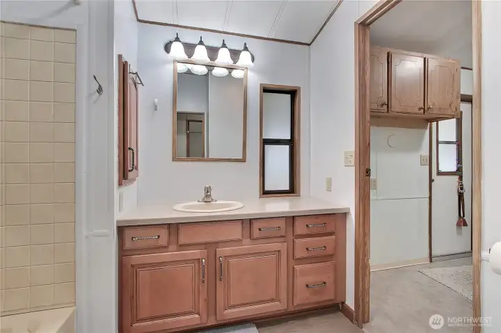 Full bath view, opens to hall and utility room for convenience, tub to bathe the grandkids! Love the cabinetry and solid-surface vanity.