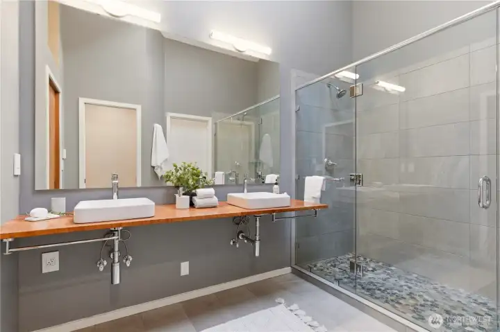 The primary bathroom has been tastefully updated, featuring a two-sink vanity, walk-in dual-head shower, and heated tile floors.