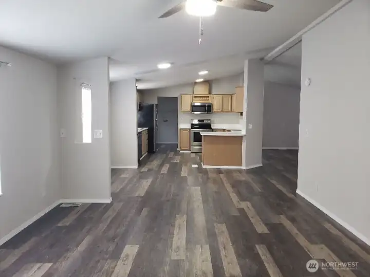 Another Opposite View Picture of the Huge Kitchen Showing Ample Cabinet Space, Newer Counter Tops, LED Lighting, All Stainless Appliances Including Built In Microwave, Glass Top Stove Oven, Trim, and Vinyl Plank Flooring Looking into the Kitchen And Ding Room from the Second Living Room.