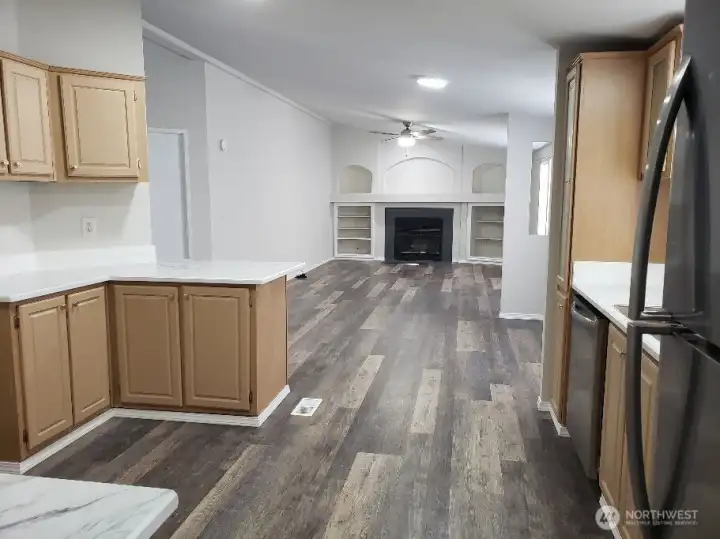 Another Opposite View Picture of the Huge Kitchen Showing Ample Cabinet Space, Newer Counter Tops, LED Lighting, All Stainless Appliances Including Built In Microwave, Glass Top Stove Oven, Trim, and Vinyl Plank Flooring Looking into the Kitchen And Ding Room from the Second Living Room.