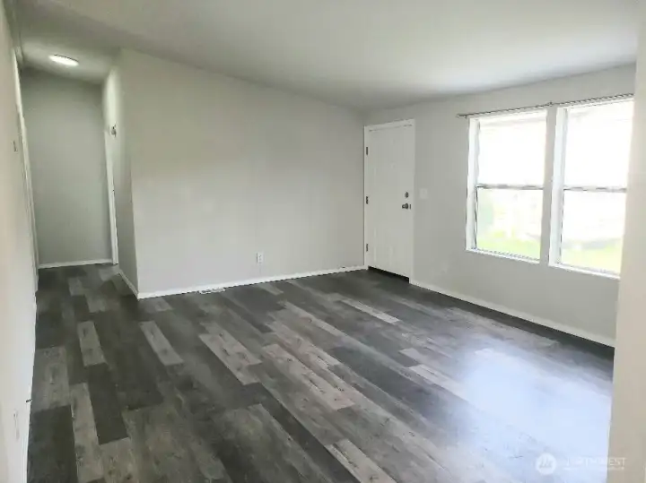 Opposite Picture of the Enormous Main Living Room Showing the Front Door Entry, the Vinyl Plank Flooring and Newer Paint and Trim Looking at the Hallway.