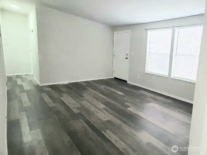 Opposite Picture of the Enormous Main Living Room Showing the Front Door Entry, the Vinyl Plank Flooring and Newer Paint and Trim Looking at the Hallway.
