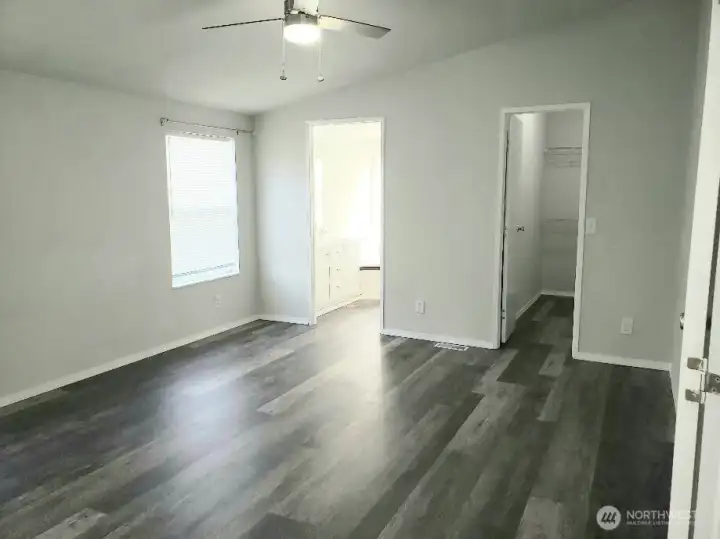 An Opposite View of the Huge Primary Master Bedroom from the Double Entry Doors Showing Newer Trim, and Vinyl Plank Flooring and Looking at the Primary Bath Room and Walk In Closet.