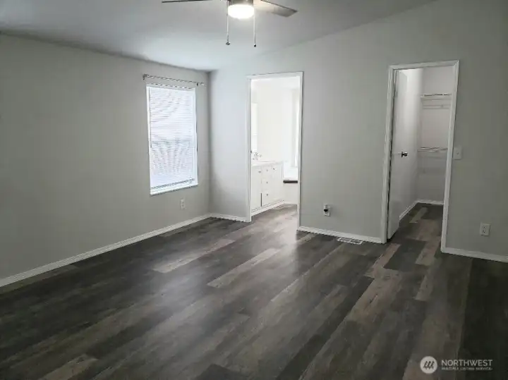 An Opposite View of the Huge Primary Master Bedroom from the Double Entry Doors Showing Newer Trim, and Vinyl Plank Flooring and Looking at the Primary Bath Room and Walk In Closet.