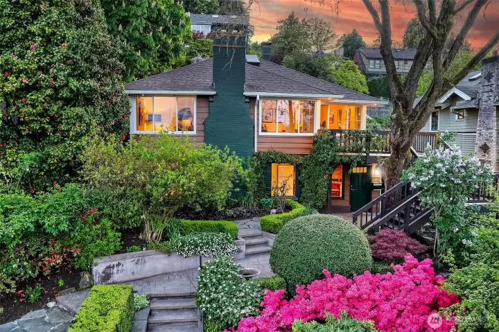 View of the front of the house with flowering gardens and deck stairs up to the main level.
