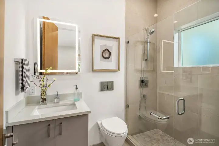 Main level primary suite ensuite bathroom with heated floors, European wall-mounted toilet, and lighted mirror