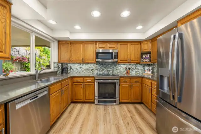 Efficient U-Shaped Kitchen with LVP flooring, SS Appliances, Solid Wood Cabinets, Quartz Counters and Tile Backsplash.  The Double Window Above the Sink Overlooks the Gorgeous Side Yard.
