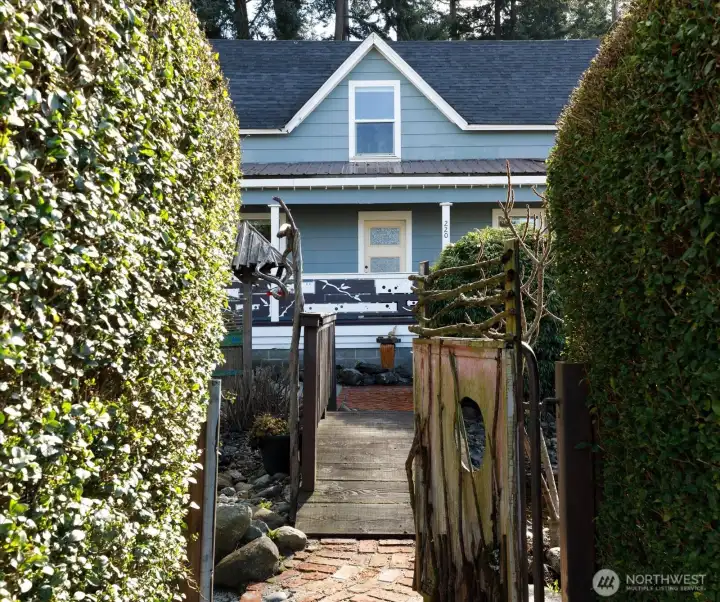 A whimsical garden bridge and rustic gate lead to a lovely garden retreat.
