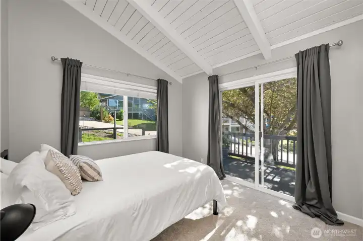 Third bedroom with vaulted ceilings, soft natural light, and direct deck access for enjoying fresh air and surrounding greenery.