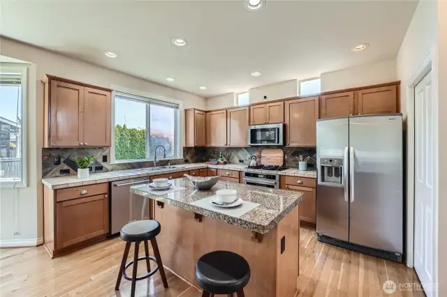 This beautifully appointed kitchen is a chef’s dream, featuring sleek granite countertops, warm wood cabinetry, and a stylish tile backsplash. Stainless steel appliances—including a gas range, built-in microwave, and side-by-side refrigerator—offer both functionality and modern appeal. A central island provides additional prep space and casual seating, ideal for entertaining or enjoying a quick meal. Large windows and upper transom windows flood the space with natural light, enhancing the airy ambiance. Thoughtfully designed for both beauty and efficiency, this kitchen is the perfect blend of form and function.
