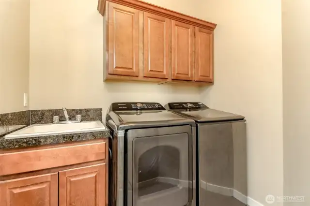 Practical upstairs laundry room with utility sink and storage cabinets