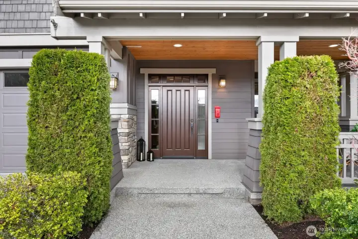 Covered front entry with rich wood front door, cedar soffits, stone accents, and elegant Craftsman details creates a warm first impression for this luxury Kirkland home.