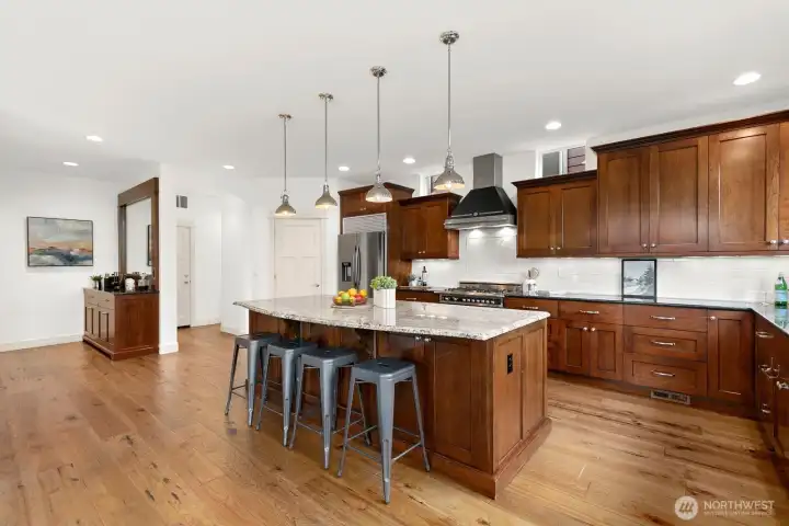 Chef's kitchen features custom wood cabinetry, oversized granite island, stainless steel appliances, gas range with professional hood, abundant storage, and generous prep space.