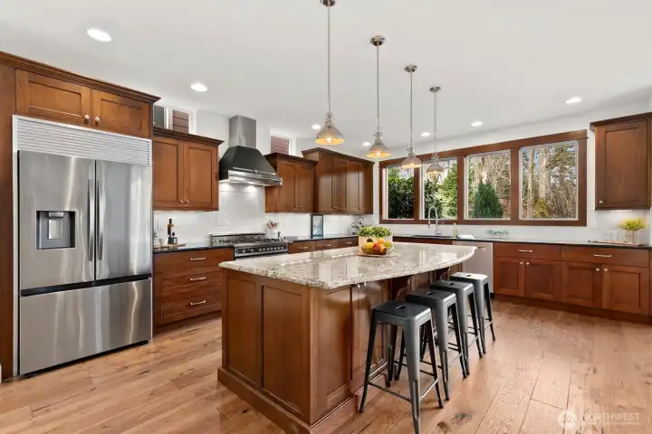 Spacious gourmet kitchen with extensive cabinetry, granite countertops, large center island, subway tile backsplash, and oversized windows overlooking the peaceful backyard.