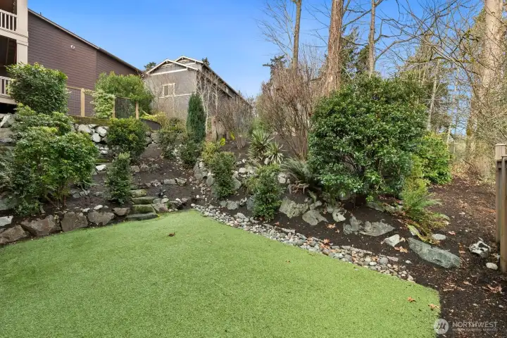 Beautifully designed backyard with mature plantings, natural stone accents, and a private setting backing to lush greenery.