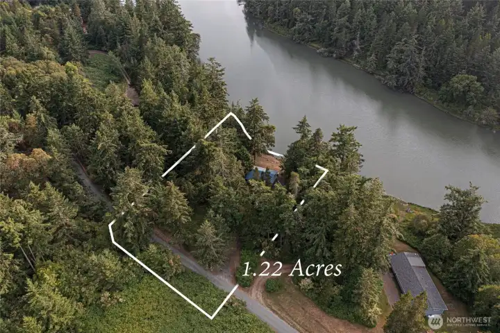 Aerial view highlighting the approximately 1.22-acre property with a private setting surrounded by mature evergreens and waterfront along Mitchell Bay.