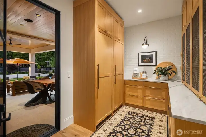Walk-in pantry features a Thermador column freezer, lots of storage, brick backsplash, quartzite countertops, and metal-mesh screens on cabinet fronts.