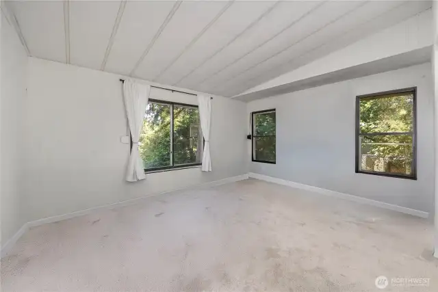Primary bedroom w/ lots of windows and new carpeting.