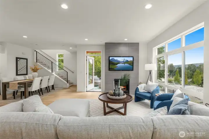 Spacious great room anchored by a modern gas fireplace and oversized windows with lush views.