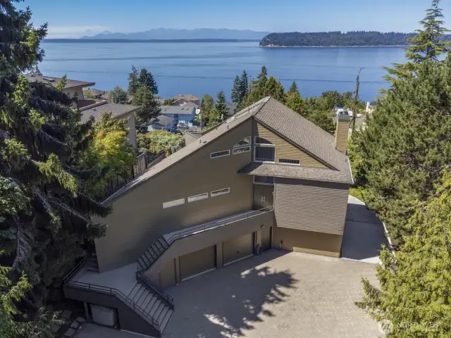 The rear of the home has the parking. The stairs up to the walkway bring you to the formal entry. The door below on the driveway level is convenient for everyday use.