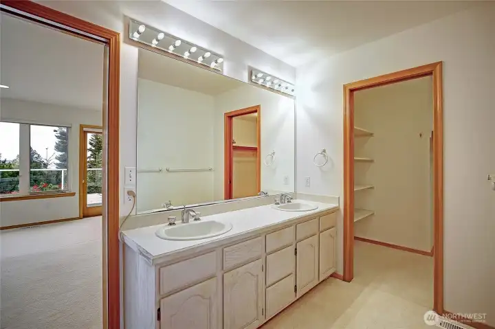 Bathroom with double sinks off primary bedroom with closet space.
