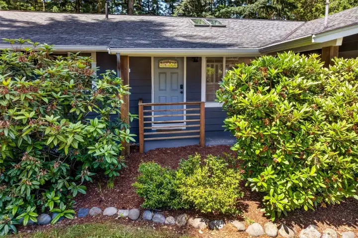 A covered, railed entry framed by mature rhododendrons creates a welcoming arrival, and the stained-glass transom above the front door adds character from the first step.