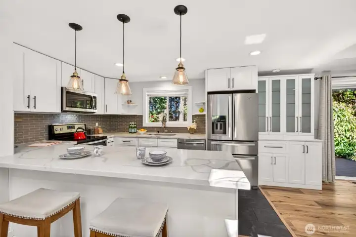 A quartz-topped peninsula with seating and a window framing the wooded surroundings make this updated kitchen as functional as it is inviting.