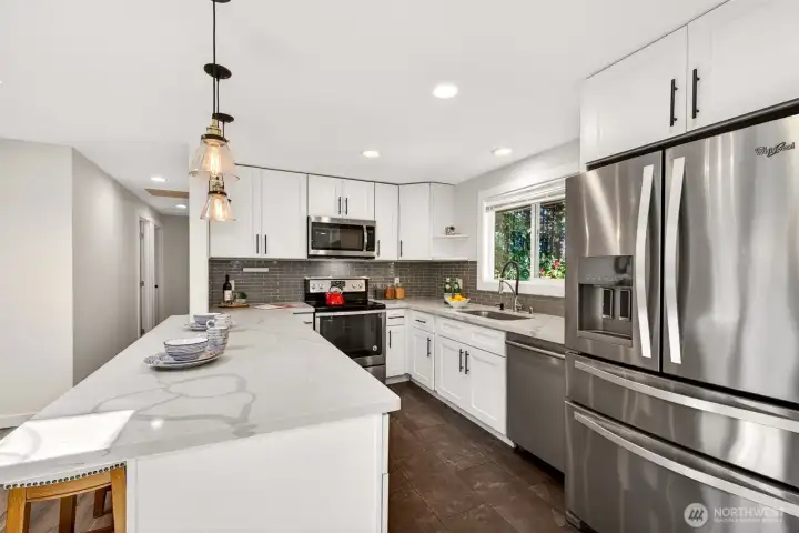 White shaker cabinetry, quartz counters, and stainless appliances make this updated kitchen a pleasure to cook in, while the window above the sink frames the surrounding greenery and the hallway leads conveniently to the bedrooms.