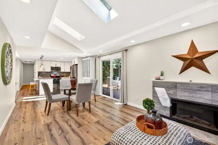 Vaulted ceilings and skylights crown an open layout where the kitchen, dining, and living areas flow together, with the fireplace and deck slider giving the central space both warmth and a connection to the backyard.