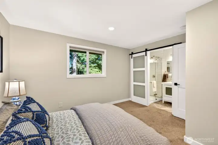 This bedroom enjoys direct access to the updated bath through a sliding barn door, with a window framing the evergreen surroundings for a peaceful start to each day.