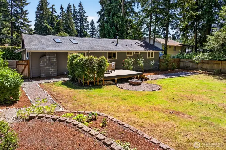 The generous, level backyard offers established garden beds, a lawn, and a fire pit, providing ample room to garden, relax, or simply enjoy the privacy of the tree-lined setting.