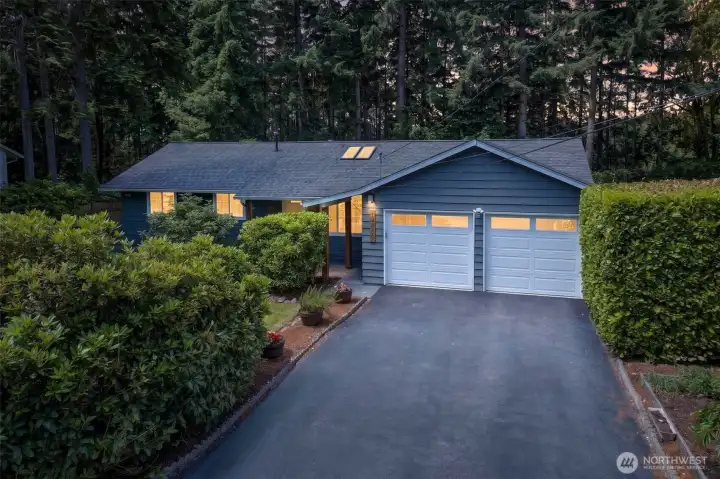 The attached two-car garage and long driveway provide ample parking, while flanking hedges and a soft evening glow give the home a welcoming, secluded feel at day's end.