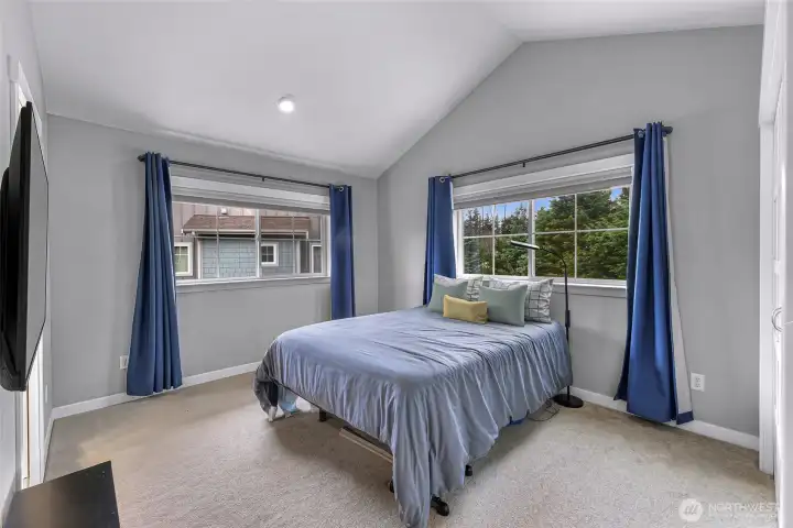 Bright primary bedroom with vaulted ceilings and large windows that offer peaceful views of the treetops.