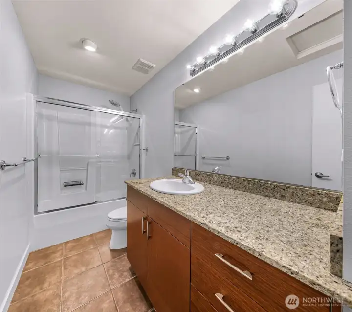 Bright second full bathroom with an extended granite vanity, updated lighting, and a clean tub and shower combo.