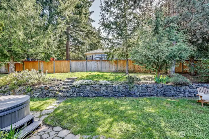 The backyard is flat, with established trees and a hot tub. Plenty of space for entertaining here!