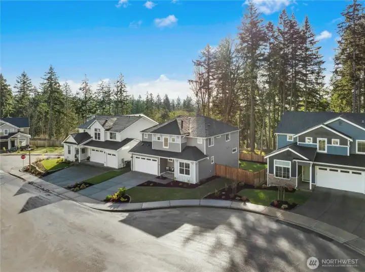 This aerial perspective showcases the home’s ideal setting—tucked along a quiet curve in a thoughtfully designed neighborhood, bordered by mature evergreens that create a natural sense of privacy and serenity. The backdrop of protected greenery offers a rare, peaceful contrast to newer construction, while the cohesive streetscape reflects pride of ownership throughout the community. It’s the best of both worlds: a modern neighborhood feel with the timeless beauty of the Pacific Northwest just beyond your doorstep.