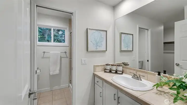 Primary bath highlighted by tile floors and countertops and freshly painted cabinetry.