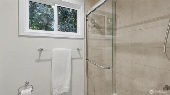 New large glass shower in primary suite with well positioned window to let in light yet maintain privacy