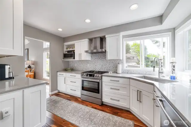 A custom chef’s kitchen anchors the home with quartz countertops, premium appliances, custom cabinetry, and electronic blinds over the sink