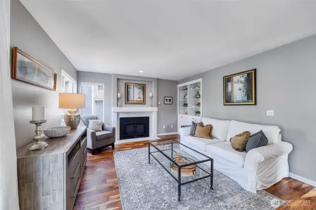 Inviting living room features engineered hardwood floors, a cozy fireplace, and built-in shelving for added charm and function