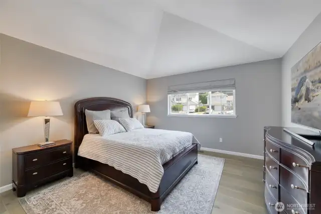 Serene primary bedroom features vaulted ceilings, elegant engineered hardwood flooring, and abundant natural light