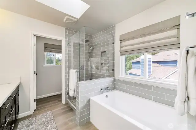 Spa-inspired primary bath features large subway tile, a frameless glass shower, and a deep soaking tub for ultimate relaxation