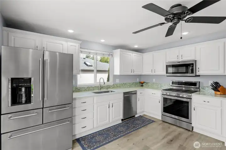 Updated kitchen featuring quartz countertops, stainless steel appliances, gas range, painted cabinetry, tile backsplash, and an undermount sink.