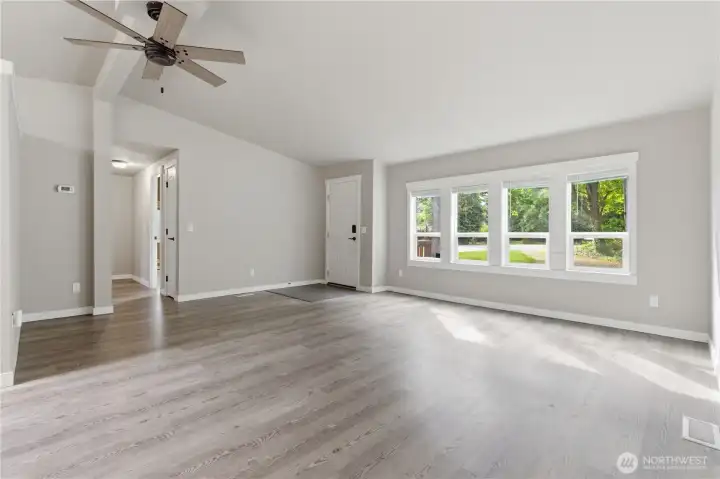 Entry is tiles and adjoins with durable plank flooring. Inside the front door you will be amazed at the bank of windows that provides consistent natural lighting.  Ceiling fan and vaulted ceiling. This room has white trimmed windows and casing and windows that vent from the bottom.  Blinds are on each of the windows. The hallway to the left leads to the hallway closet, 2nd bath and two bedrooms.
